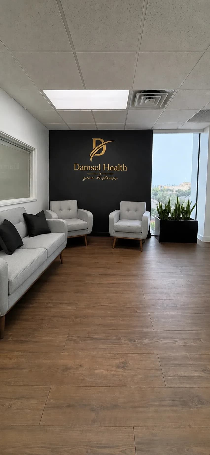 Damsel Health waiting room — lounge seating in front of a brand wall with the Damsel Health logo